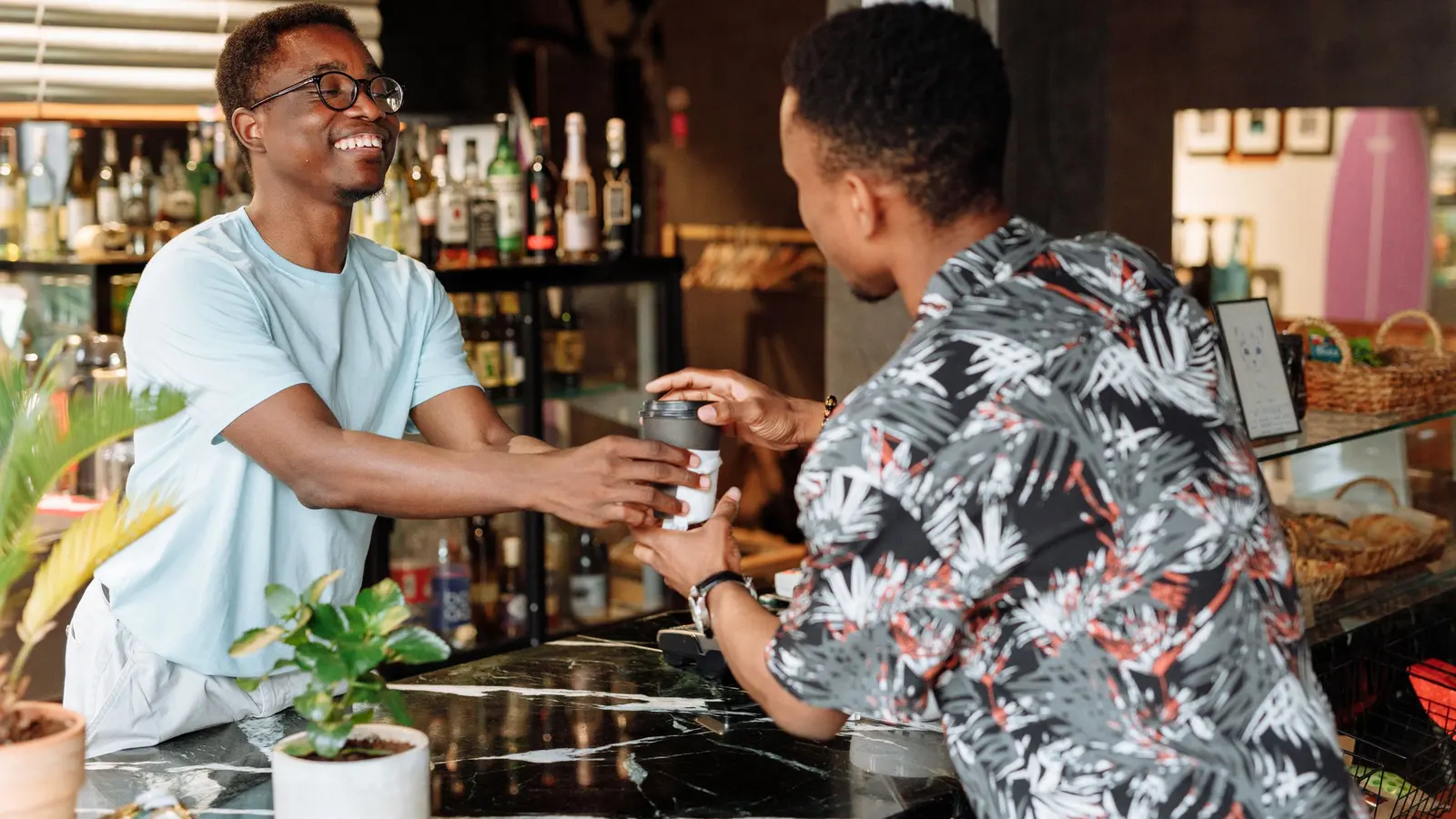 Un commerçant tend un café à un client par-dessus le comptoir, tous deux souriants